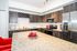 Modern kitchen with sleek dark wood cabinetry, granite countertops, stainless steel appliances, and vibrant red accent chairs.