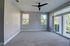 Bright and inviting room with plush carpet, modern ceiling fan, and large windows offering lush green views.