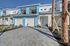 Modern townhouse facade with vibrant blue accents, featuring spacious driveways and lush landscaping under clear blue skies.