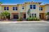 Charming two-story townhouse exterior with vibrant yellow facade, lush landscaping, and a double car garage, perfect for modern living.