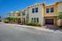Charming townhouse exterior with vibrant yellow facade, lush landscaping, and elegant architecture under a bright blue sky.