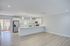 Modern open-plan kitchen with sleek white cabinetry, stainless steel appliances, and large island, complemented by elegant pendant lighting and expansive wood flooring.