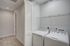 Modern laundry area featuring sleek white washer and dryer units, ample shelving space, and elegant louvered doors.
