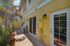 Charming exterior side view of a sunny yellow building with elegant lantern lighting and lush tropical plants on a paved path.