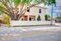 Charming two-story home with a white picket fence and lush greenery, nestled under a large, majestic tree in a peaceful neighborhood.