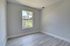 Bright, modern apartment room with large window, light gray walls, and elegant wood flooring.