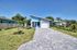 Charming modern house with a sleek blue and white exterior, single-car garage, and lush green lawn surrounded by tropical landscaping.