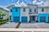 Contemporary townhouse with vibrant blue accents, featuring individual garages and lush greenery under a clear sky.