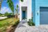 Striking modern home exterior with vibrant blue accents, lush palm trees, and a welcoming entryway.