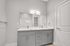 Elegant bathroom featuring dual sinks, sleek gray cabinetry, modern lighting, and a spacious mirror.