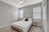 Bright and inviting bedroom with modern decor, featuring a comfortable double bed, cozy lighting, and ample natural light from two large windows.
