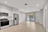 Modern open-concept living and kitchen area with sleek stainless steel appliances, wooden flooring, and large sunlit windows.