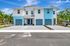 Modern duplex with tropical landscaping featuring vibrant blue accents and spacious driveways under a sunny sky.