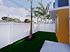 Charming outdoor corner with a lush green space, enclosed by a modern white fence, featuring a tropical palm tree and vibrant architectural accents.