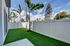 Beautiful fenced backyard with lush green artificial turf and tall palm trees under a clear blue sky.