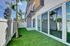 Modern apartment exterior with lush artificial turf, tall palm tree, and sleek glass doors leading to a private patio.