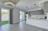 Modern open-plan kitchen and living area showcasing sleek gray cabinetry, contemporary lighting fixtures, and an inviting view to the outdoor space.