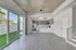 Modern open-plan kitchen and living area with sleek flooring, stylish pendant lighting, and expansive glass doors leading to a private outdoor space with lush greenery.