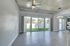 Modern living space with sleek wooden flooring, expansive glass doors, and stylish ceiling fan, leading to lush green outdoor area.