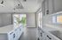 Sleek modern kitchen with elegant white cabinetry, large island, and ample natural light from floor-to-ceiling windows overlooking lush greenery.