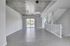 Contemporary open-plan living space with sleek gray flooring and industrial-style concrete ceiling, complemented by modern lighting and abundant natural light from large glass doors.