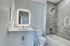 Modern bathroom with sleek marble tile, illuminated mirror, elegant fixtures, and a spacious bathtub for relaxation.