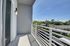 Modern balcony with sleek white railing offering a serene view of lush greenery and suburban rooftops under a clear blue sky.