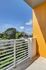 Charming balcony view with vibrant yellow accent wall, overlooking lush greenery under a bright blue sky.