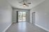 Bright and spacious room featuring elegant wood flooring, a modern ceiling fan, and sliding glass doors leading to a sunlit balcony with a serene view.