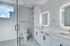 Sleek modern bathroom featuring dual vanities with illuminated mirrors, elegant white cabinetry, and a luxurious walk-in shower.