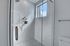 Luxurious bathroom with modern textured white wall tiles and a sleek glass shower, filled with natural light.
