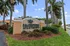 Inviting entrance to Palm Springs Apartments with lush landscaping and towering palm trees under a bright blue sky.