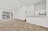 Bright and spacious living area with vaulted ceiling, carpeted flooring, and a scenic view through large windows. Open kitchen with ample cabinetry enhances the airy feel.