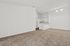 Spacious open-plan apartment with plush carpeting leading to a cozy kitchen featuring modern white cabinetry and ample lighting.