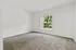Bright and airy room with plush carpeting and a large window offering lush garden views, perfect for a tranquil living space.
