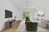 Bright and modern living room with elegant furnishings, featuring a cozy sofa, stylish chairs, and a large TV; natural light floods in through glass doors overlooking lush greenery.
