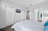 Bright and modern bedroom with plush carpeting, featuring a stylish bed, mounted flat-screen TV, and access to a sleek bathroom.