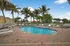 Inviting outdoor pool area with palm trees and lounge chairs under a sunny sky, perfect for relaxation.
