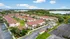 Charming apartment complex with red-roofed buildings, lush green landscaping, and ample parking under a clear blue sky.