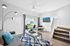 Bright and modern living room with sleek decor, featuring a glass coffee table, plush gray sofa, and vibrant blue accents; opens to a lush outdoor view through large sliding doors.