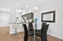 Modern dining area with a sleek glass table and elegant black chairs, adjacent to a pristine kitchen featuring ample cabinetry and bar seating.