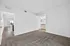 Bright and spacious room with plush carpet, open doorway view to kitchen and sunlit living area, and adjacent bathroom with modern fixtures.