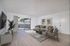 Bright and modern living room with cozy seating, sleek decor, and a view of outdoor greenery through sliding glass doors.
