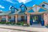 Charming apartment complex exterior with brick pillars, sleek blue siding, and vibrant landscaping under a clear blue sky.