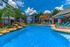 Luxurious apartment complex with a sparkling pool, stylish sun loungers, and lush landscaping under a vibrant blue sky.