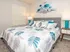 Inviting bedroom with a stylish, tufted headboard and vibrant leaf-patterned bedding, complemented by modern bedside lamps and elegant wall art.