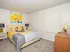 Contemporary bedroom with a plush bed, vibrant artwork, and stylish decor accents featuring a yellow and gray color scheme.