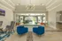 Elegant office lounge with modern furniture, blue accent chairs, and a stunning chandelier overlooking a lush outdoor view.