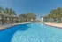 Inviting outdoor pool area with lounging chairs, shaded seating, and lush palm trees, promising relaxation and sunshine in a serene community setting.