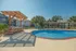 Inviting outdoor pool area with elegant pergola and sun loungers, surrounded by lush palm trees and charming apartment buildings.